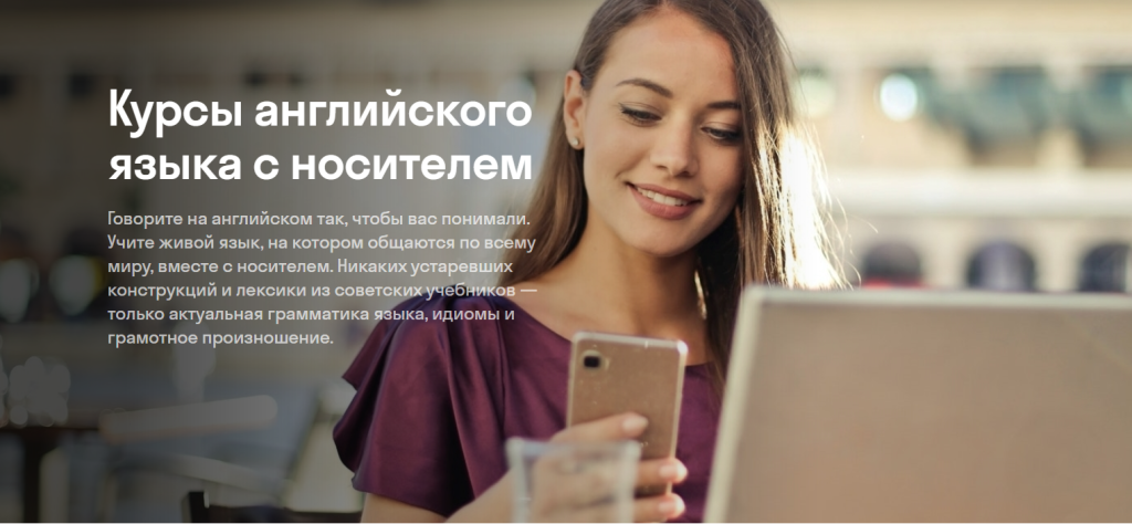 Женщина улыбается, глядя в свой смартфон, а на заднем плане появляется текст на русском языке, рекламирующий курсы английского языка.